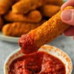 Frozen mozzarella cheese sticks cooked in air fryer being dipped in mozzarella sauce.