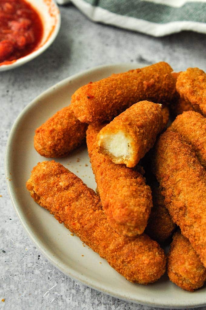 A plateful of air fryer mozzarella sticks with a bite missing from one.