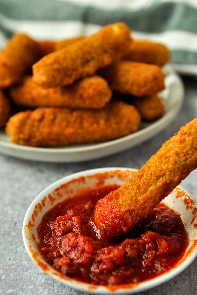 Frozen mozzarella cheese sticks cooked in air fryer being dipped in mozzarella sauce.