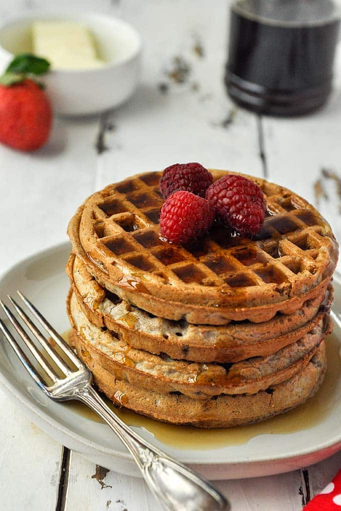 A stack of four cooked air fryer frozen waffles topped with raspberries and covered in syrup.