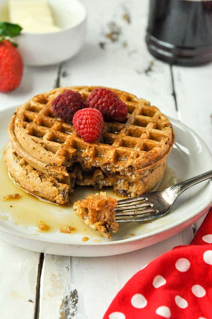 A stack of two cooked air fryer frozen waffles topped with raspberries and covered in syrup with a bite on a fork.