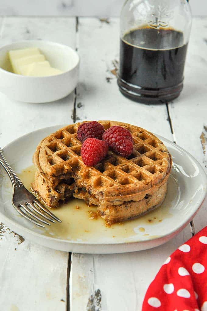 A stack of two cooked air fryer frozen waffles topped with raspberries and covered in syrup.