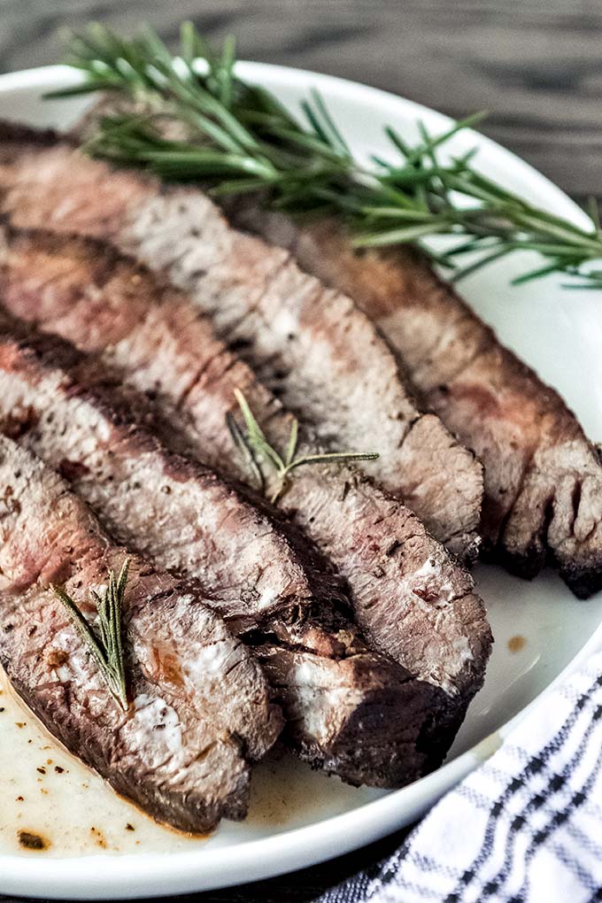 Up close plate full of cooked steak in the air fryer topped with some rosemary.