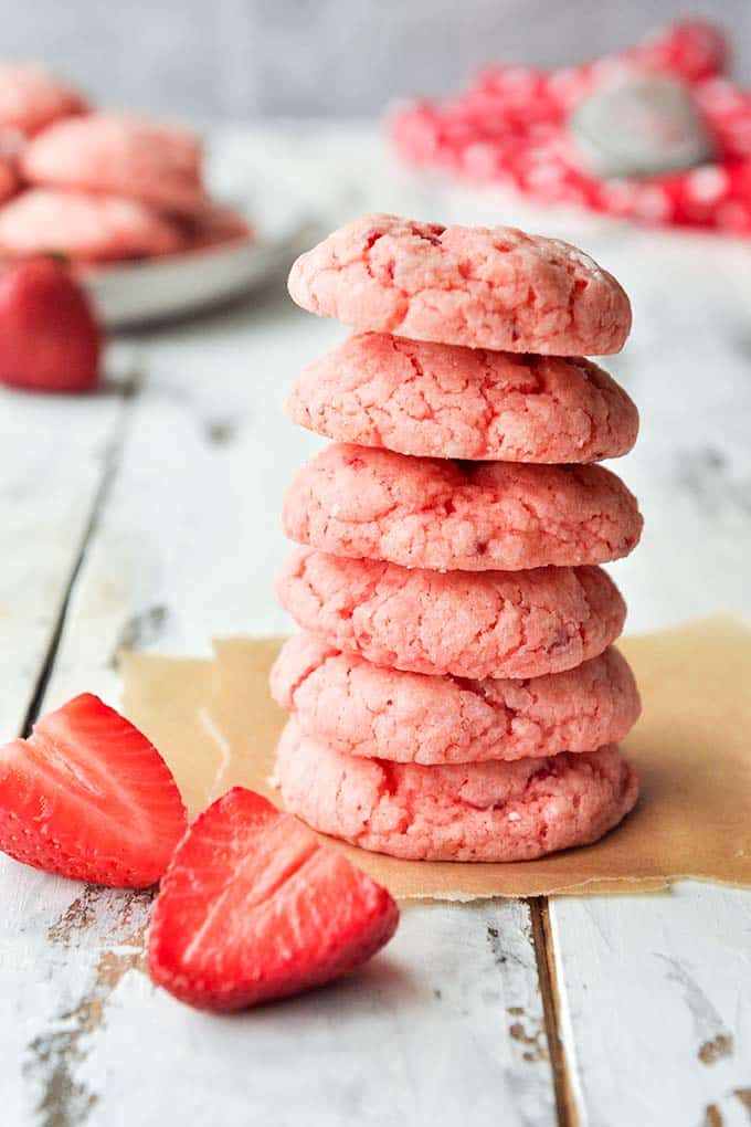 A stack of baked gooey butter cookies next to a couple cut strawberries.