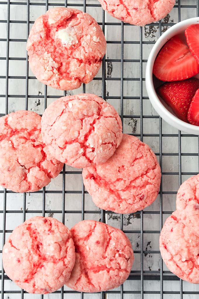 An above view of baked strawberry butter cookies with a bowl of cut strawberries.