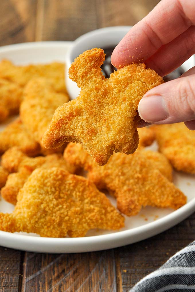 An air fryer dino nugget being held above a plateful of chicken nuggets.