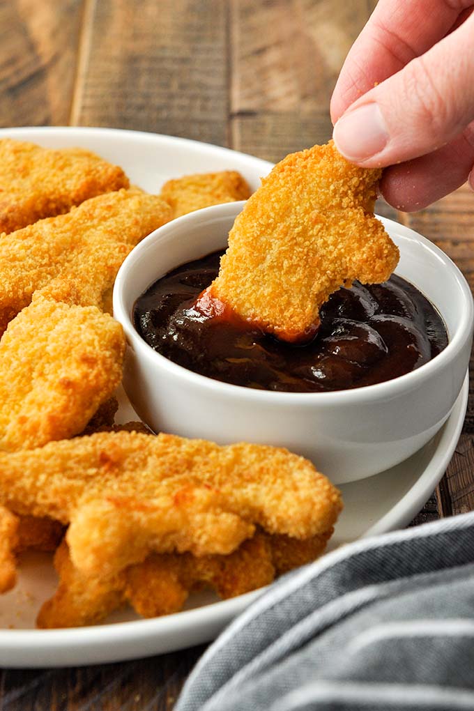 An air fryer dino nugget being dunked into dipping sauce.
