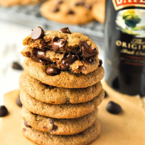 A stack of Baileys Irish cream chocolate chip cookies with a bottle of Baileys and cookies in the background.