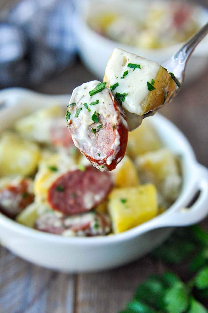 A forkful of crock pot sausage and potatoes over a bowl.
