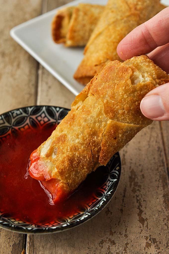 Frozen egg roll in air fryer cooked and dipping into sweet and sour sauce.