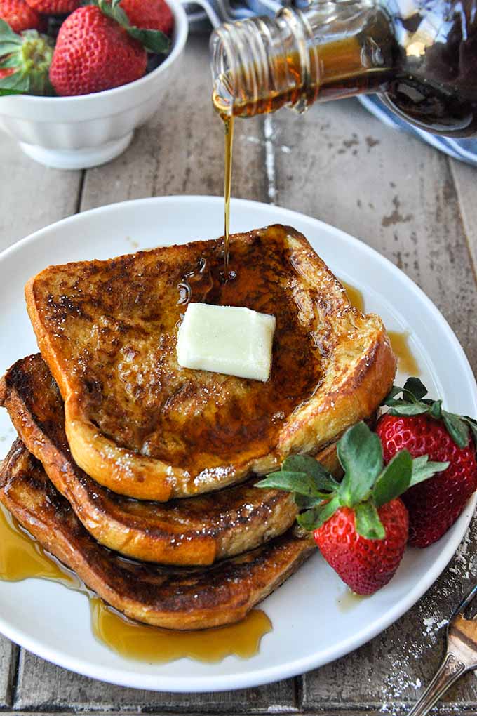 McCormick French toast stacked up on a plate with  syrup being poured on.