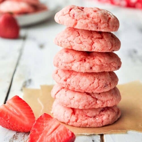 A stack of baked gooey butter cookies next to a couple cut strawberries.
