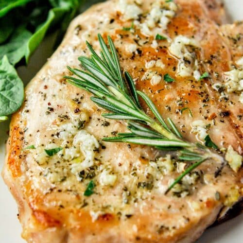 Up close of an air fryer pork chop no breading topped with a rosemary sprig.