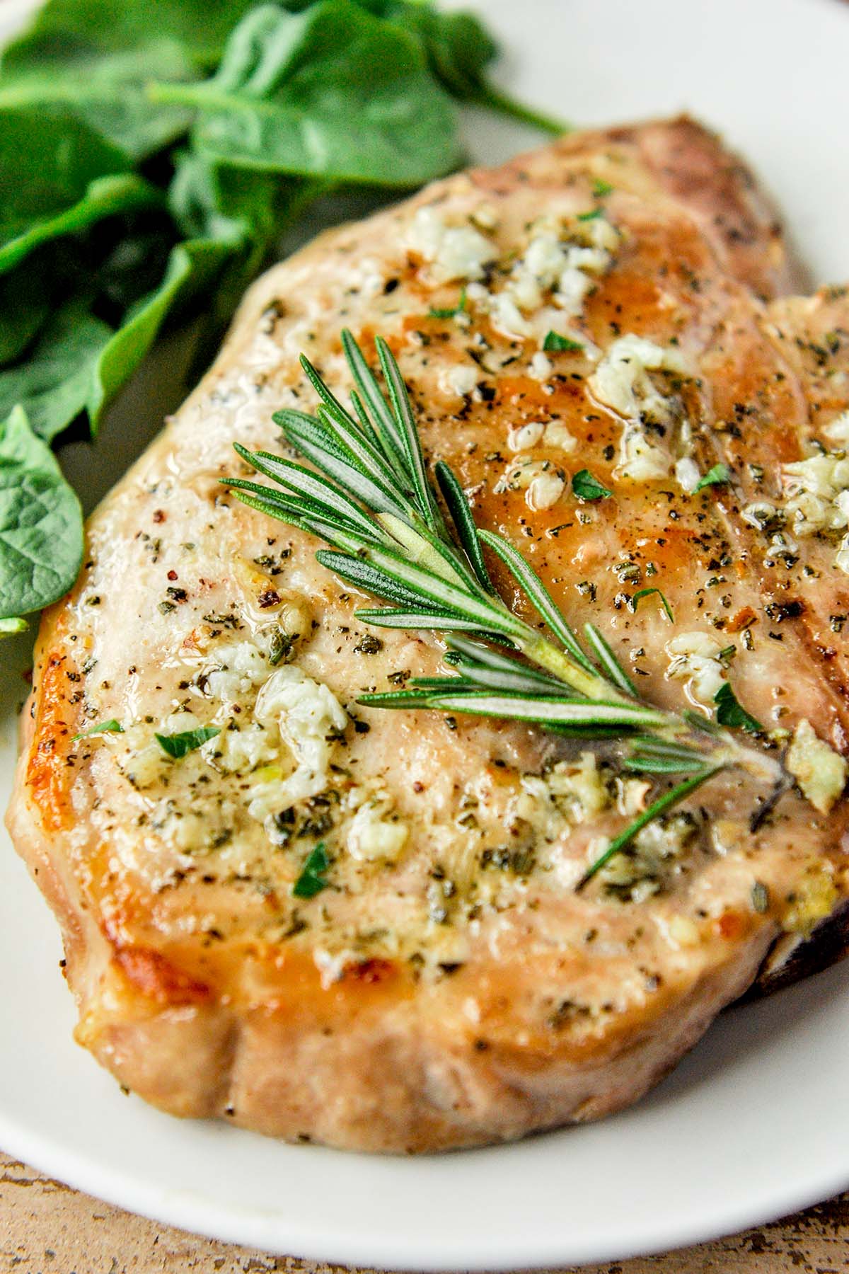 Up close of an air fryer pork chop no breading topped with a rosemary sprig.
