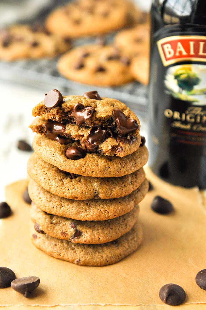 A stack of Baileys Irish cream chocolate chip cookies with a bottle of Baileys and cookies in the background.