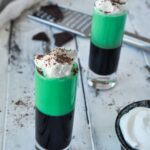 Up close of grasshopper shot topped with whipped cream and chocolate shavings with whipped cream in a small bowl.