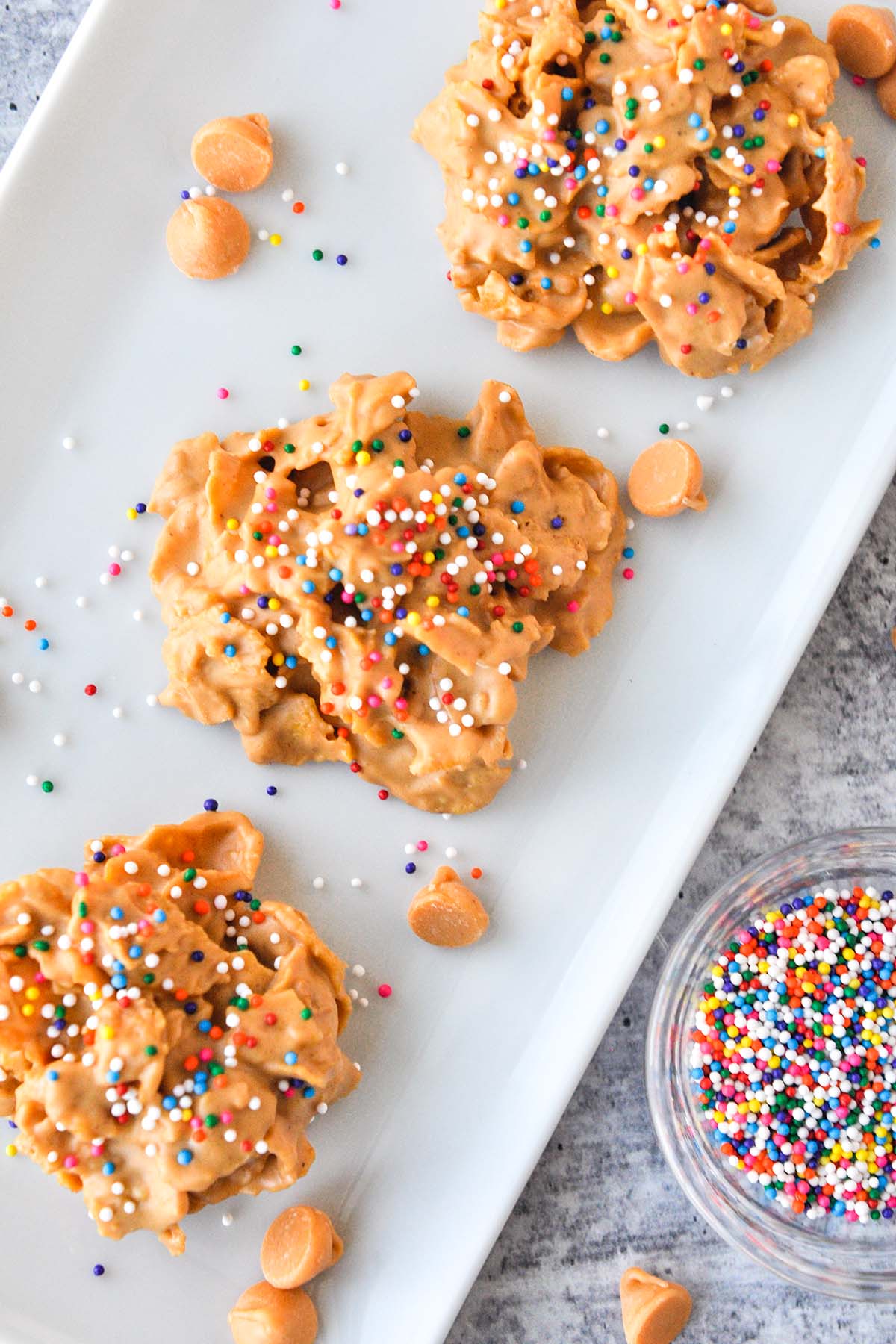 Above view of butterscotch cornflake cookies topped with sprinkles with a bowl of sprinkles.