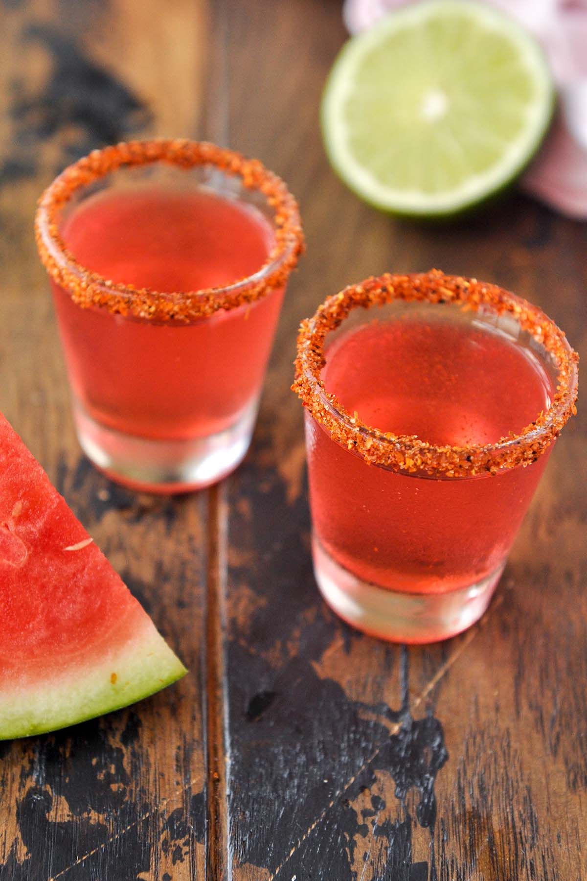 Two shot glasses of Mexican Candy Shot with a slice of watermelon.