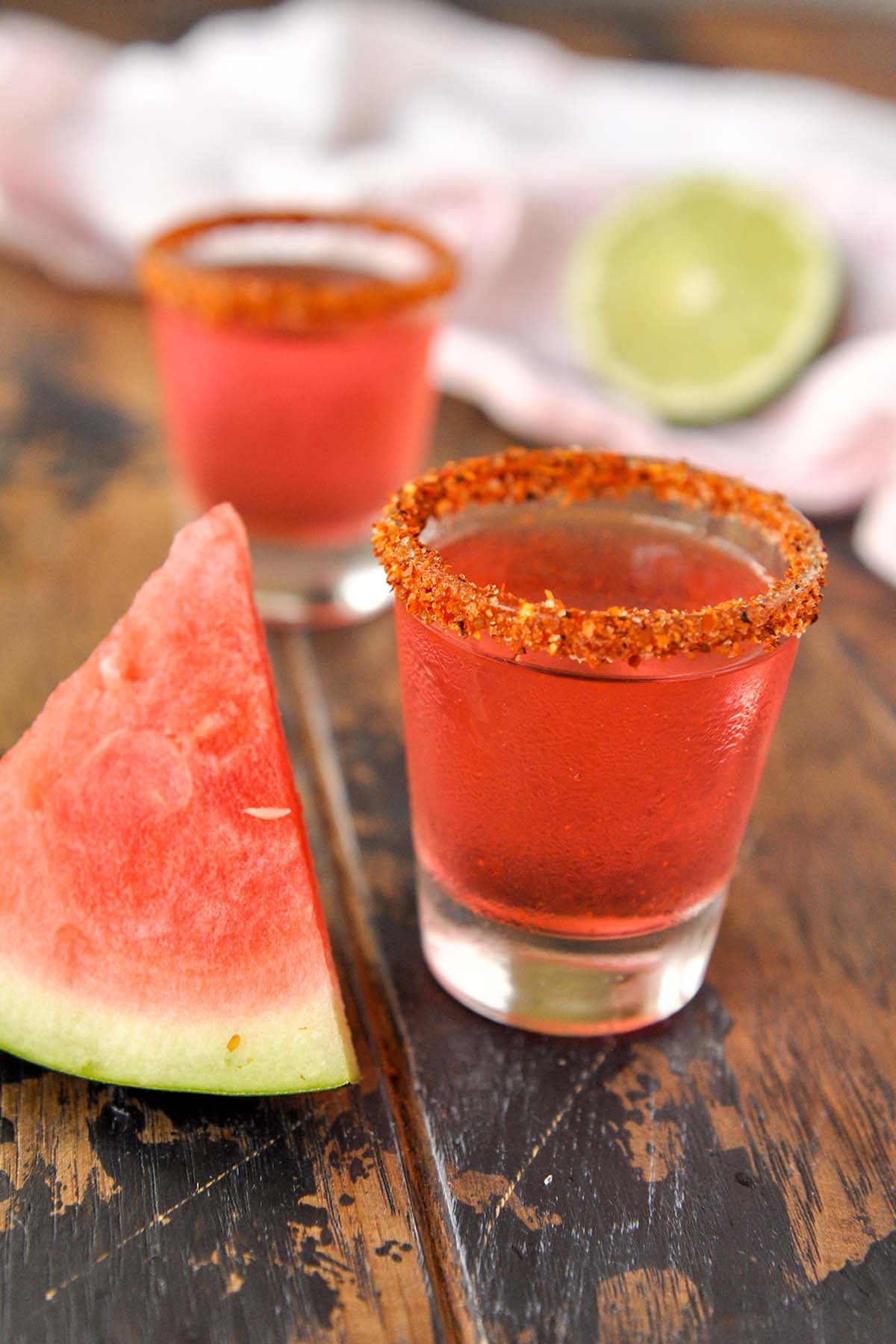 Two shot glasses of Mexican candy shot with a slice of watermelon.