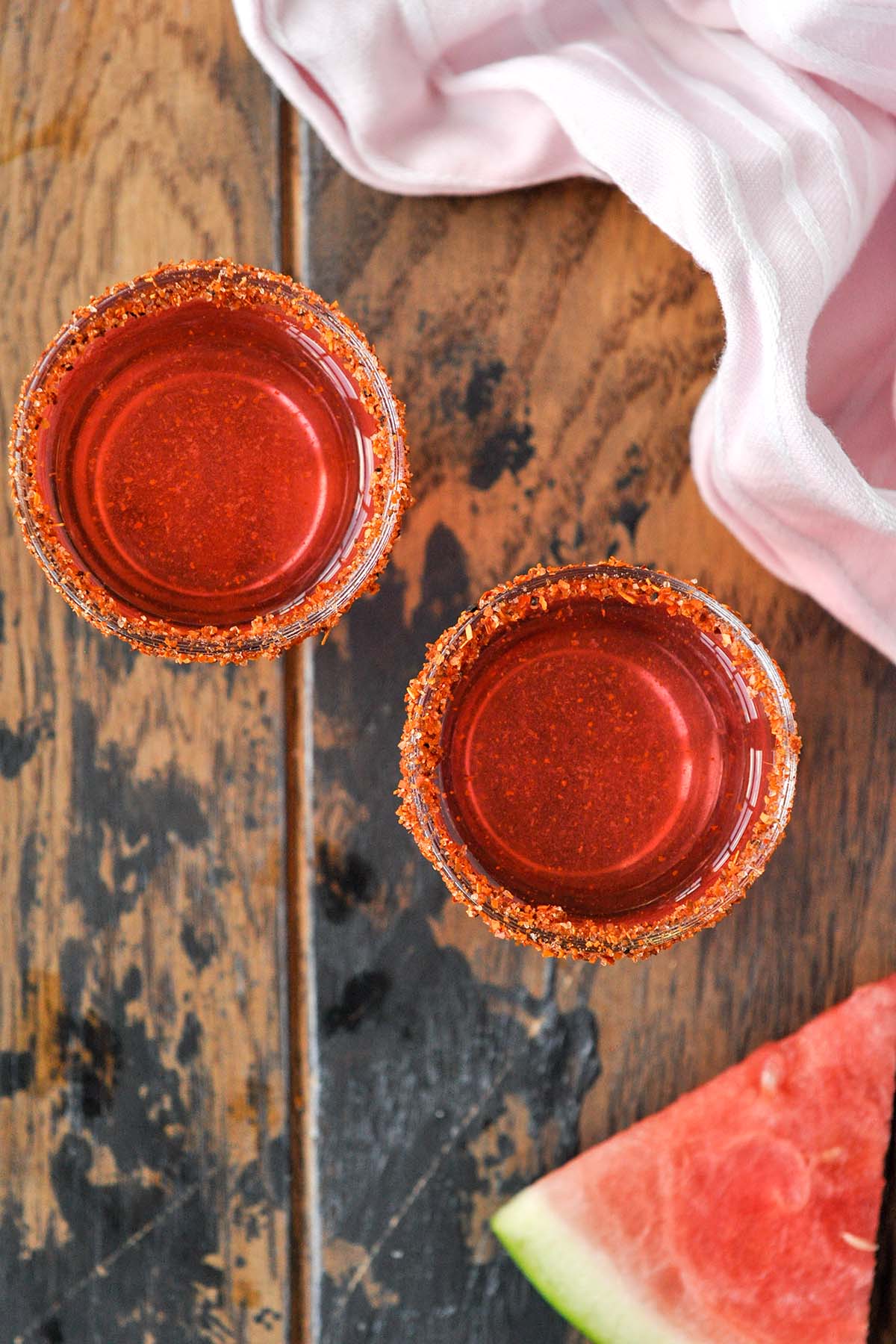 Above view of two shot glasses of Mexican candy shot with a slice of watermelon and pink towel.
