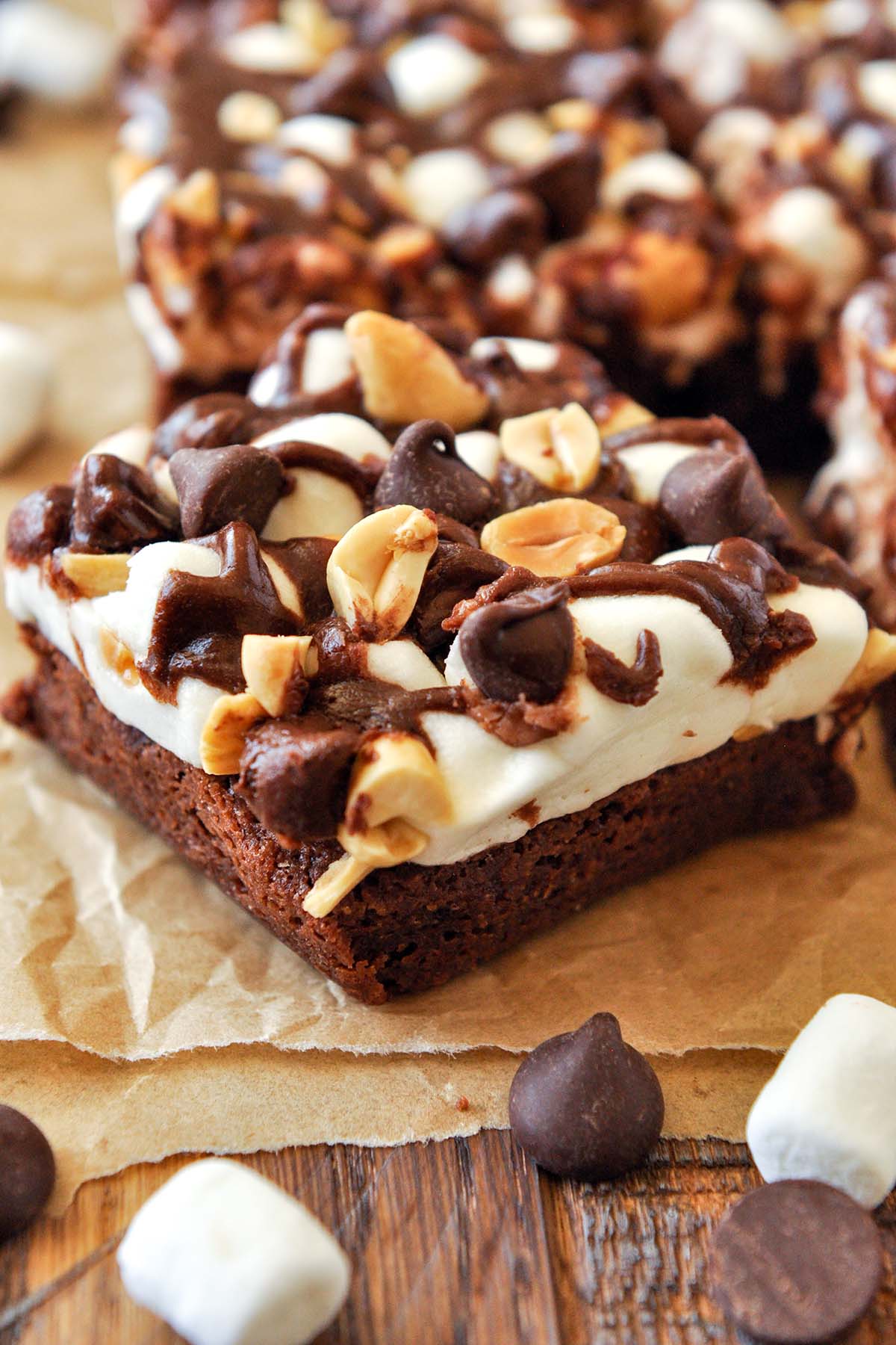 A close up of a rocky road brownie with more brownies in the background and marshmallows and chocolate chips in the foreground.
