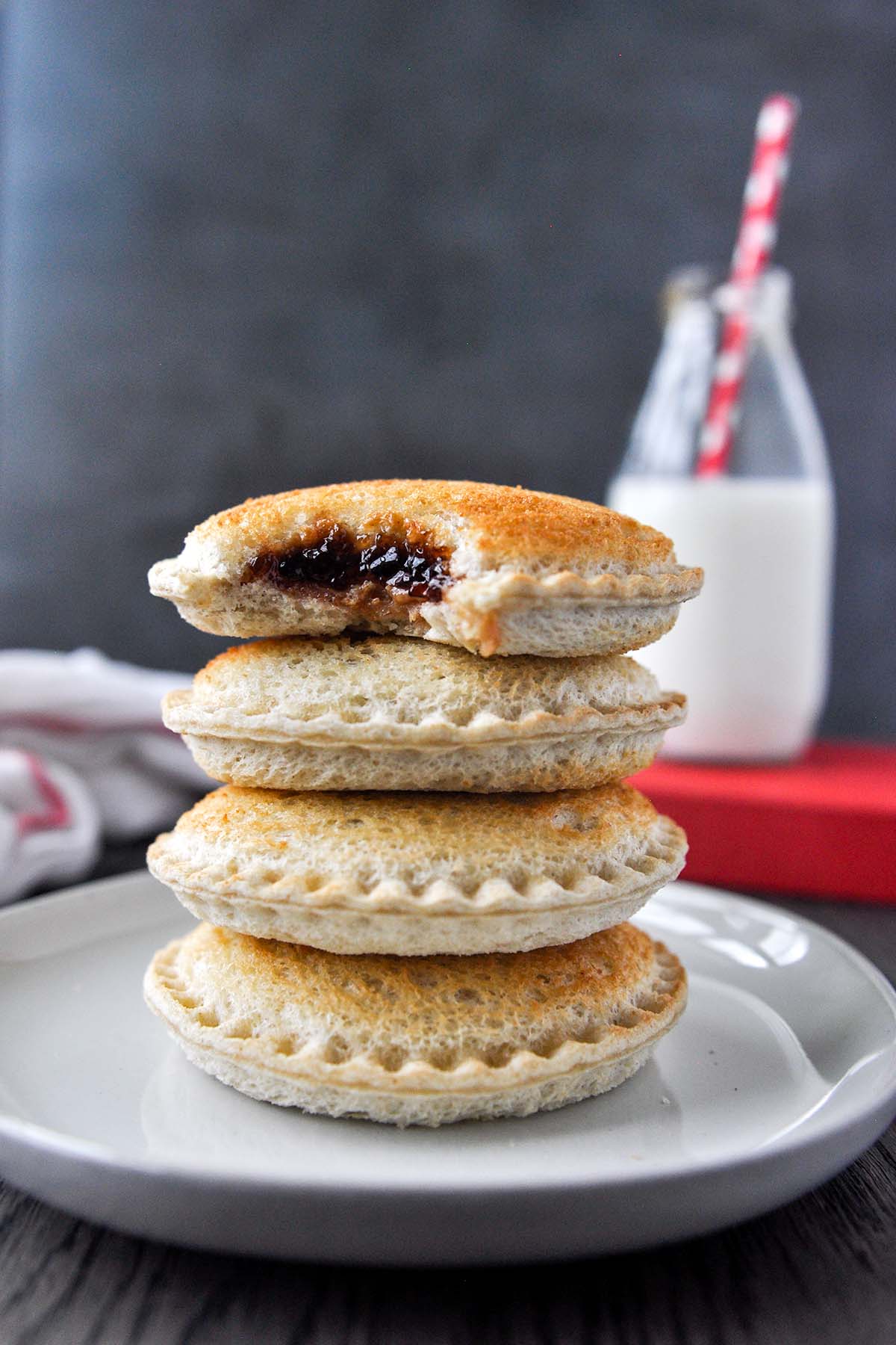 A stack of four air fried Uncrustables on a plate with a glass bottle of milk in the background.