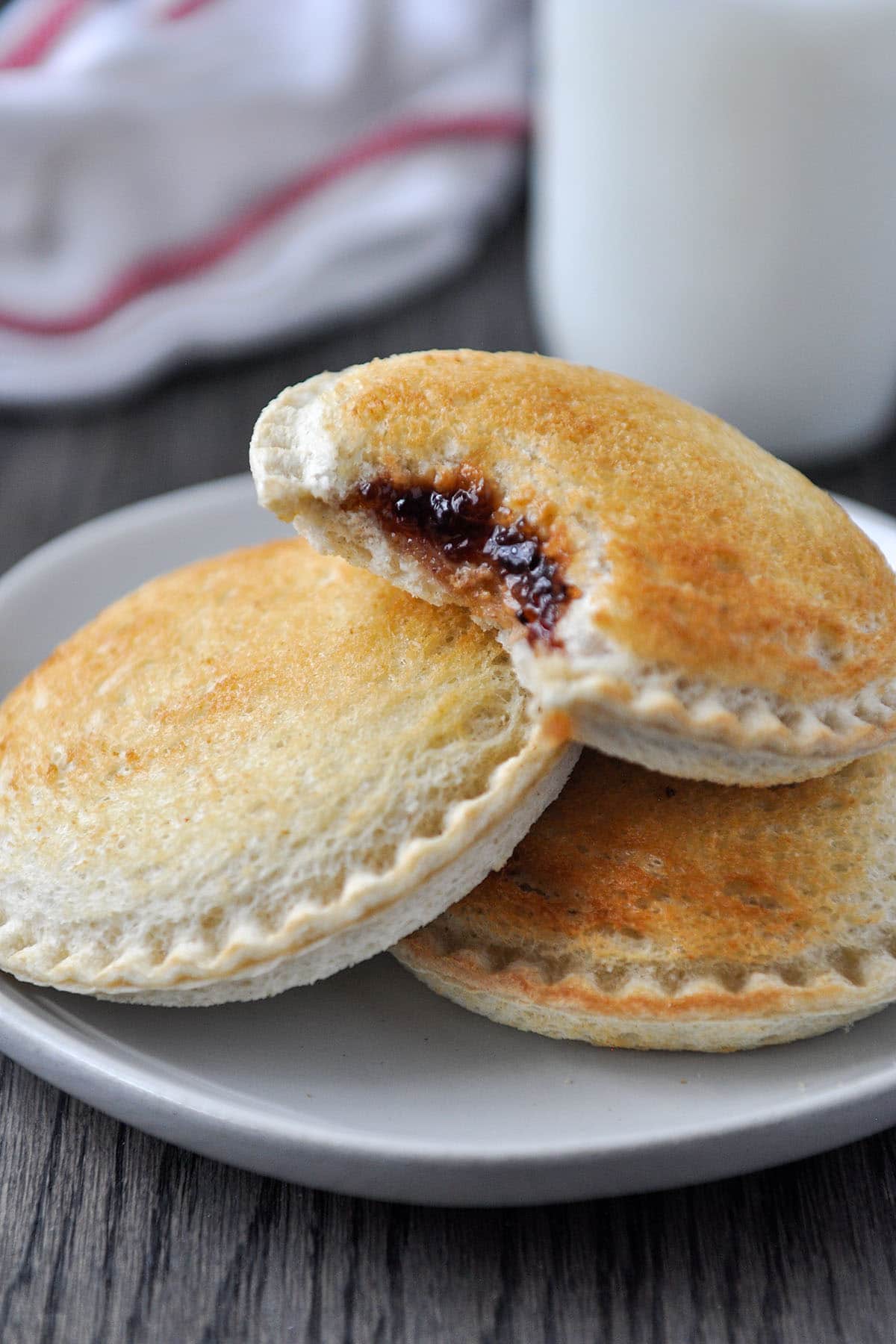 A plate of three cooked Uncrustables sandwiches, one is missing a bite so you can see the peanut butter and jelly inside.