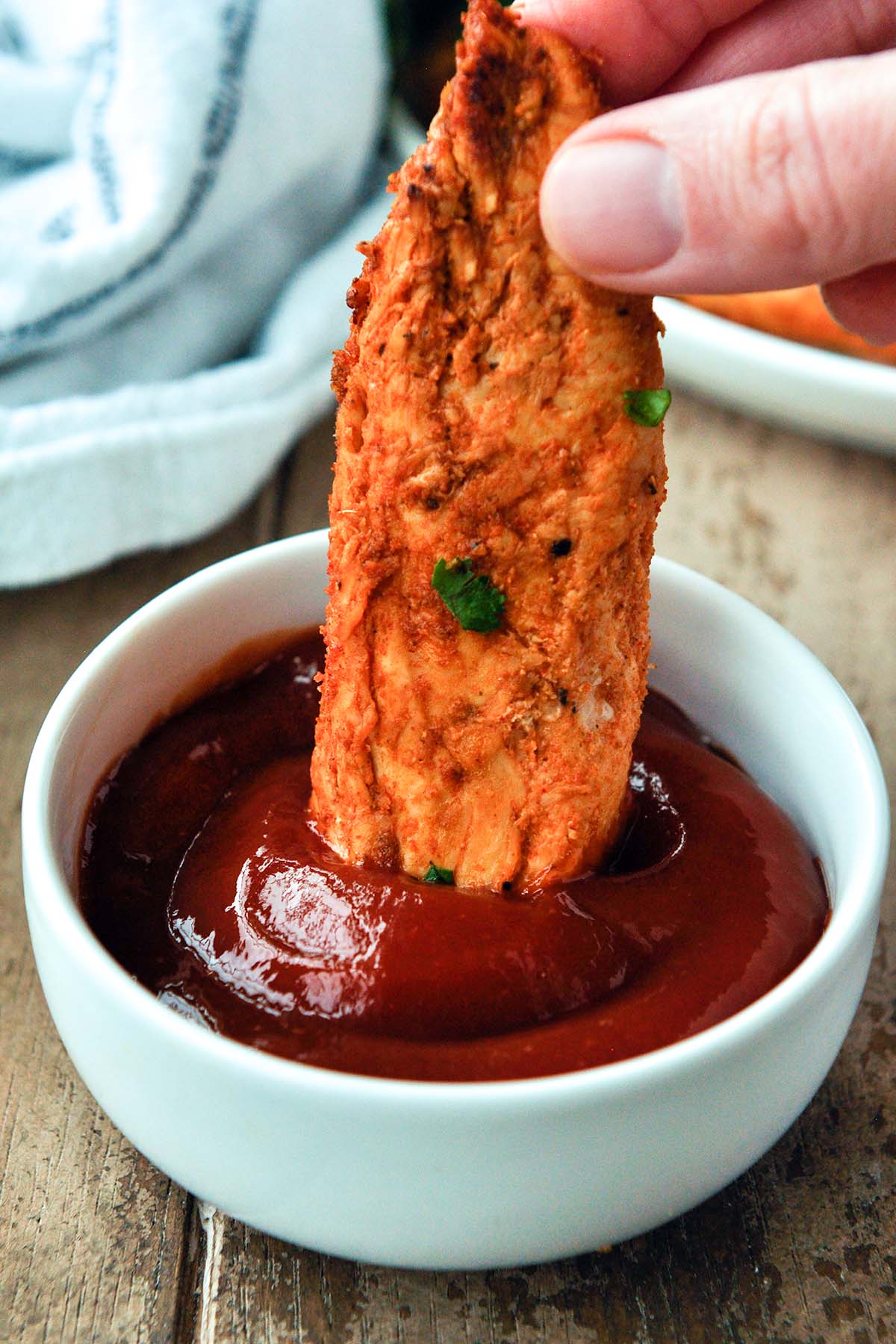 A cooked chicken tender being dipped in ketchup.