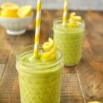 Two cups of lemon green smoothie with a twist of lemon peel and a yellow and white striped straw.