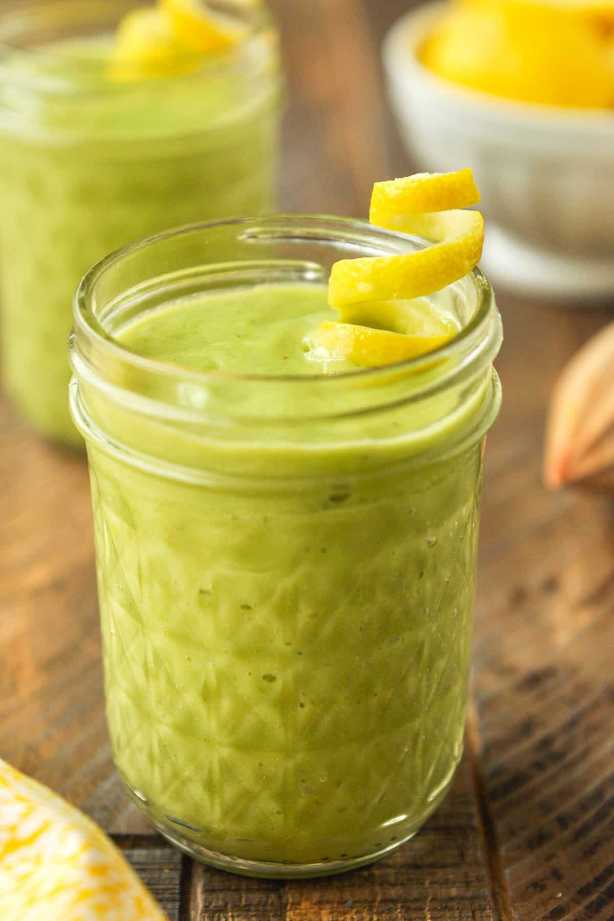 Up close of lemon green smoothie with a twist of lemon peel and a yellow and white striped straw.