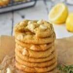 A stack of 7 cookies on a piece of parchment with white chocolate chips and lemons in the background.