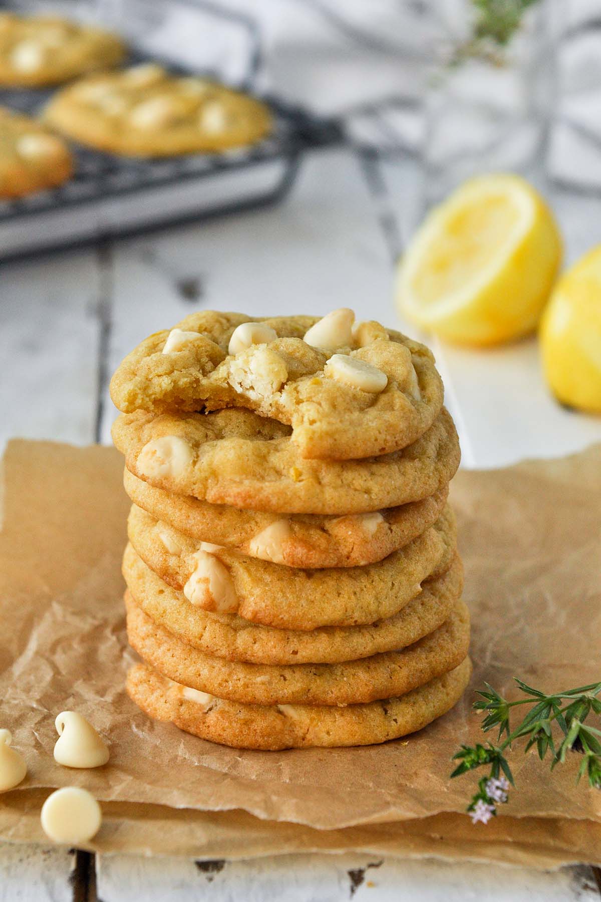 A stack of 7 cookies on a piece of parchment with white chocolate chips  and lemons in the background.