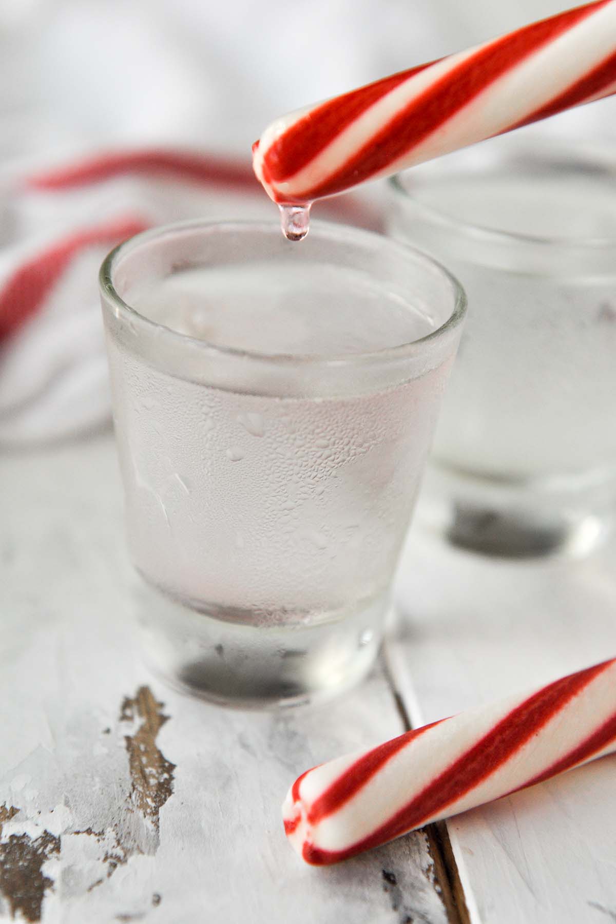 Two shot glasses of the polar bear shot with a peppermint stick above one glass with a drip coming down.