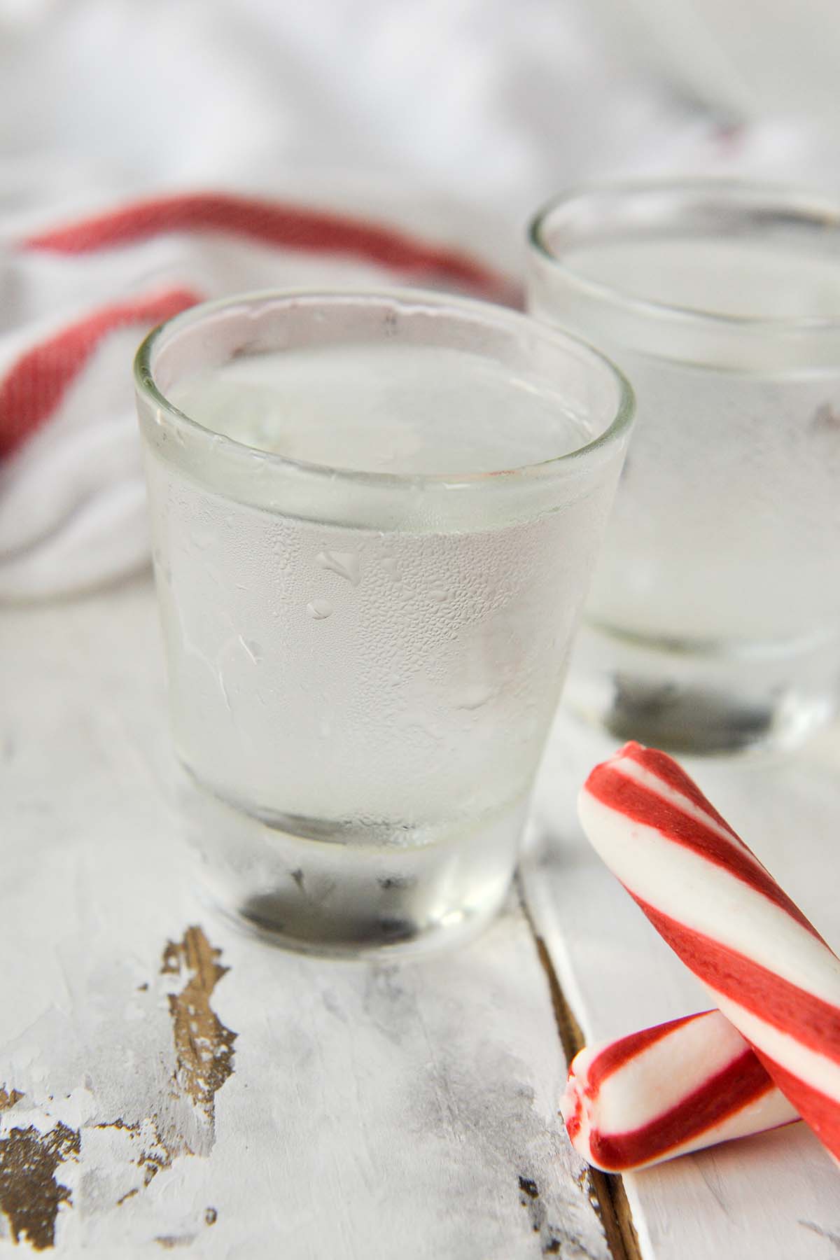 Two shot glasses of the polar bear shot with two peppermint sticks next to them.