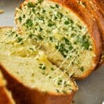Gooey strings of cheese reach between two slices of garlic bread.