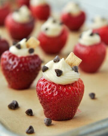 Up close of a strawberry stuffed with cheesecake filling, sprinkled with mini chocolate chips and topped with a little chunk of graham cracker.