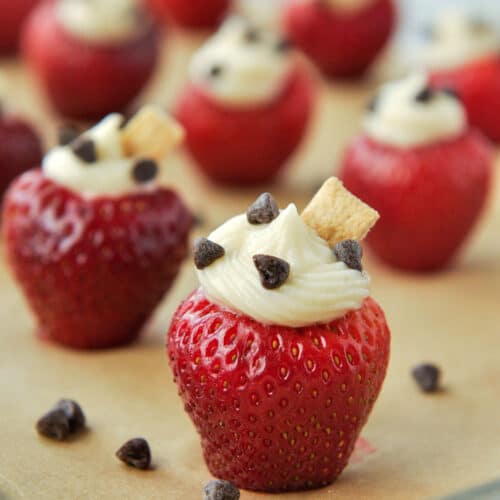 Up close of a strawberry stuffed with cheesecake filling, sprinkled with mini chocolate chips and topped with a little chunk of graham cracker.