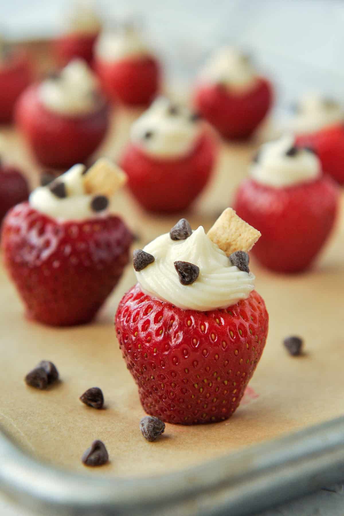 Up close of a strawberry stuffed with cheesecake filling, sprinkled with mini chocolate chips and topped with a little chunk of graham cracker.