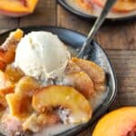 A plate full of air fryer peach cobbler topped with ice cream. Another plate in the background.