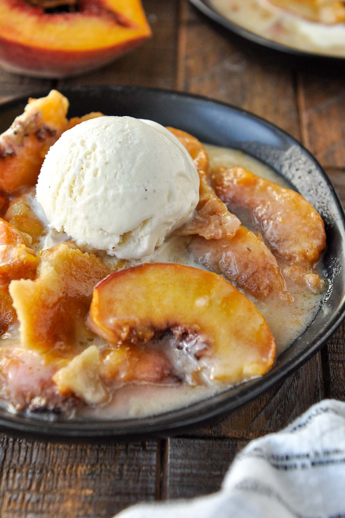 A plate full of air fryer peach cobbler topped with ice cream. Another plate in the background.
