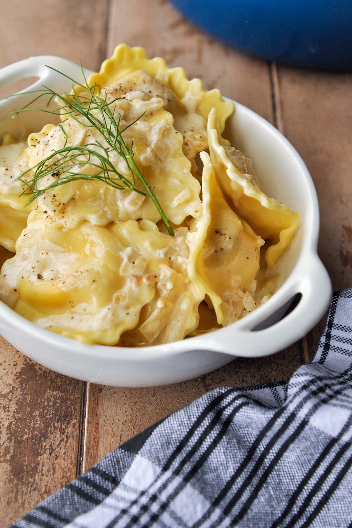 A bowl full of lobster ravioli with creamy sauce and a little sprig of fennel.