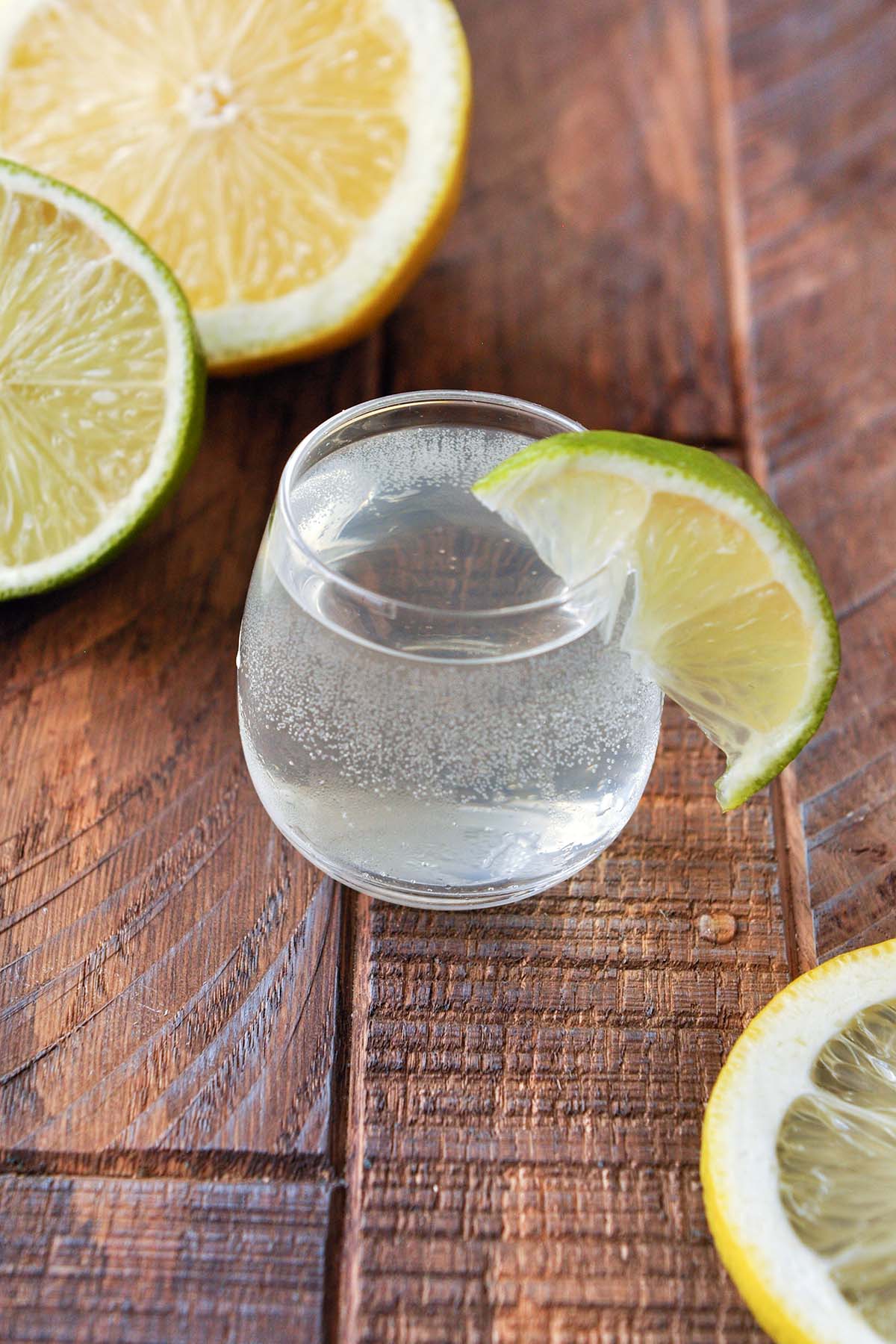 A single shot glass of the white tea shot with a lime wedge on the side of the glass and lemon and lime halves in the background.