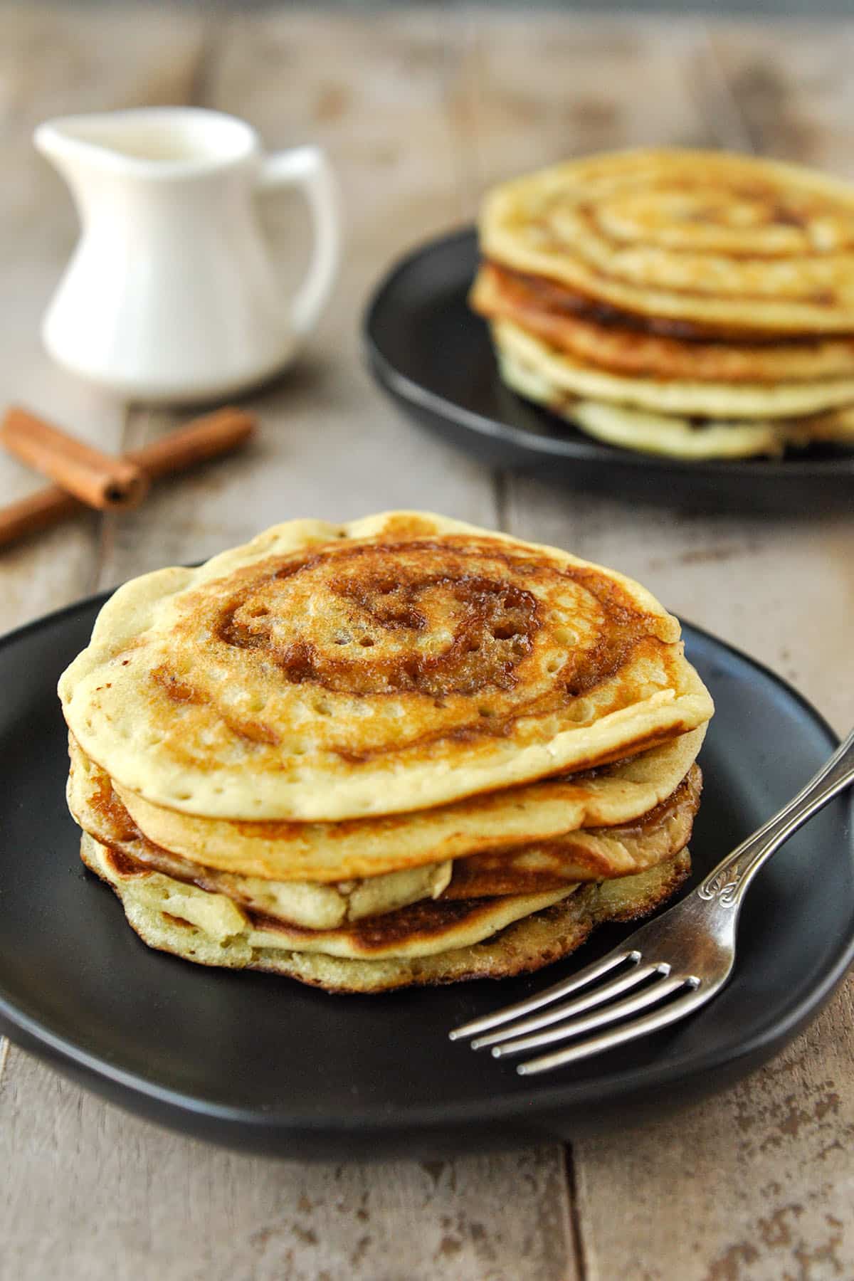 Two plates of stacks of cinnamon swirl pancakes.