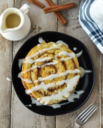 An above view of cinnamon swirl pancakes on a black plate with a drizzle of cream cheese frosting.