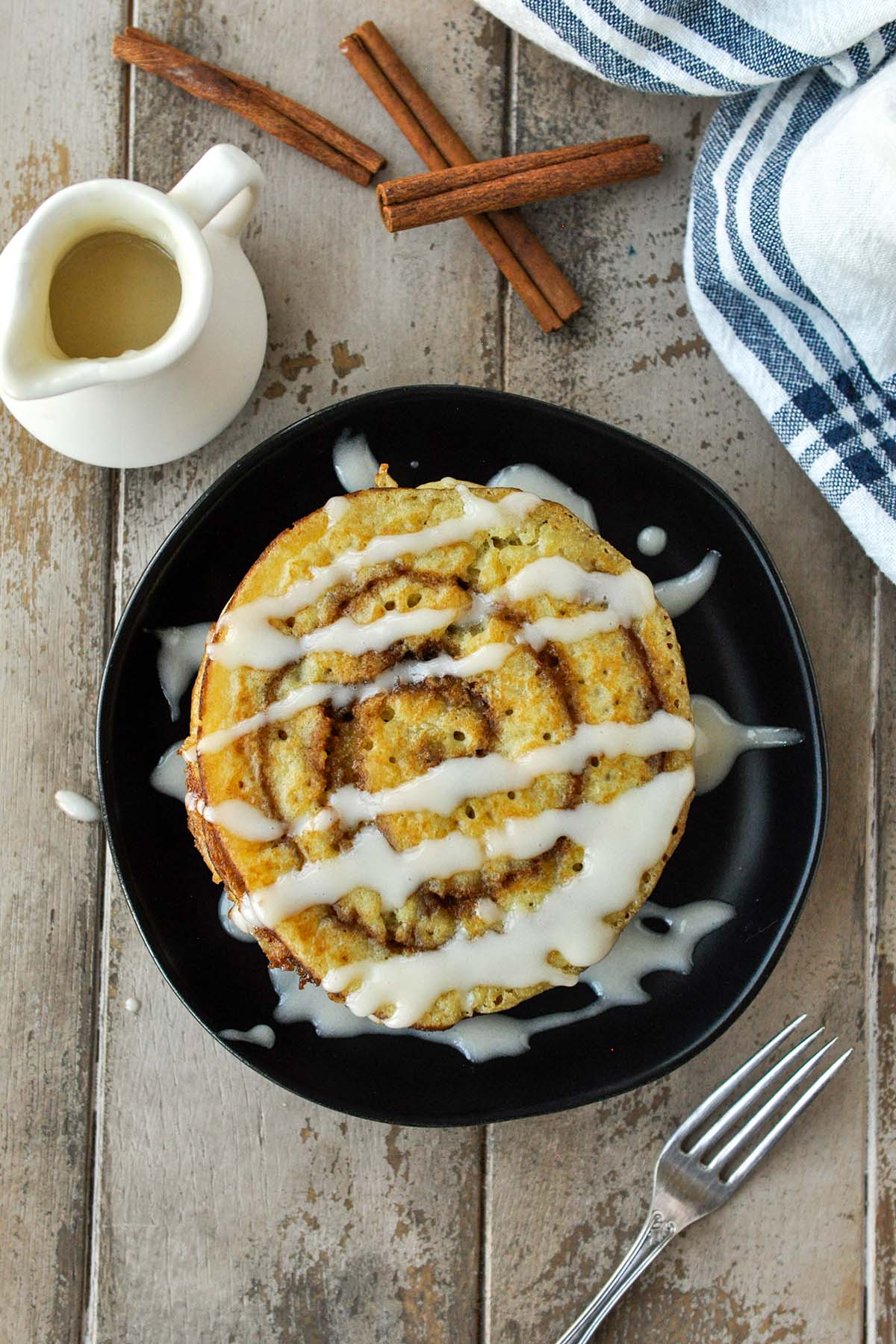 An above view of cinnamon swirl pancakes on a black plate with a drizzle of cream cheese frosting.