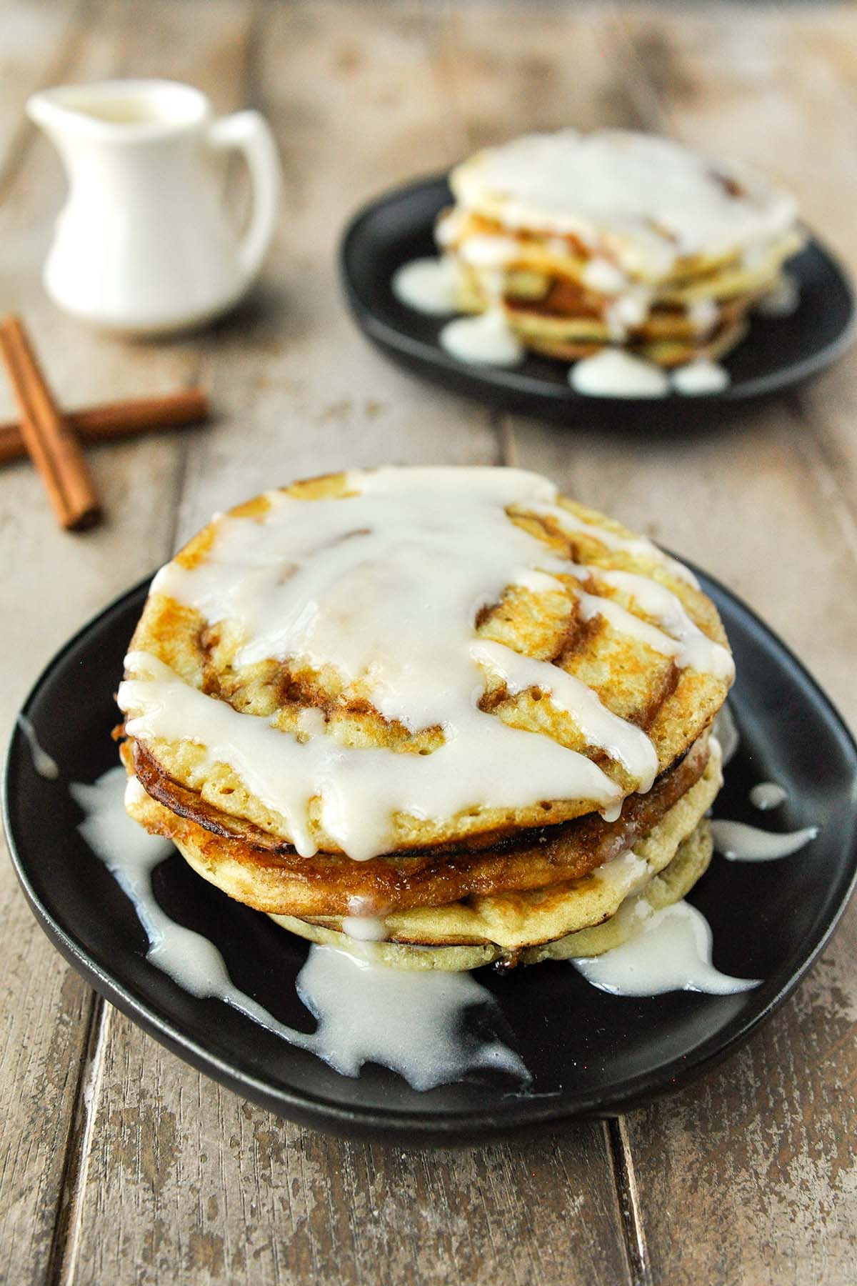 Two plates of stacks of cinnamon pancakes with cream cheese syrup.