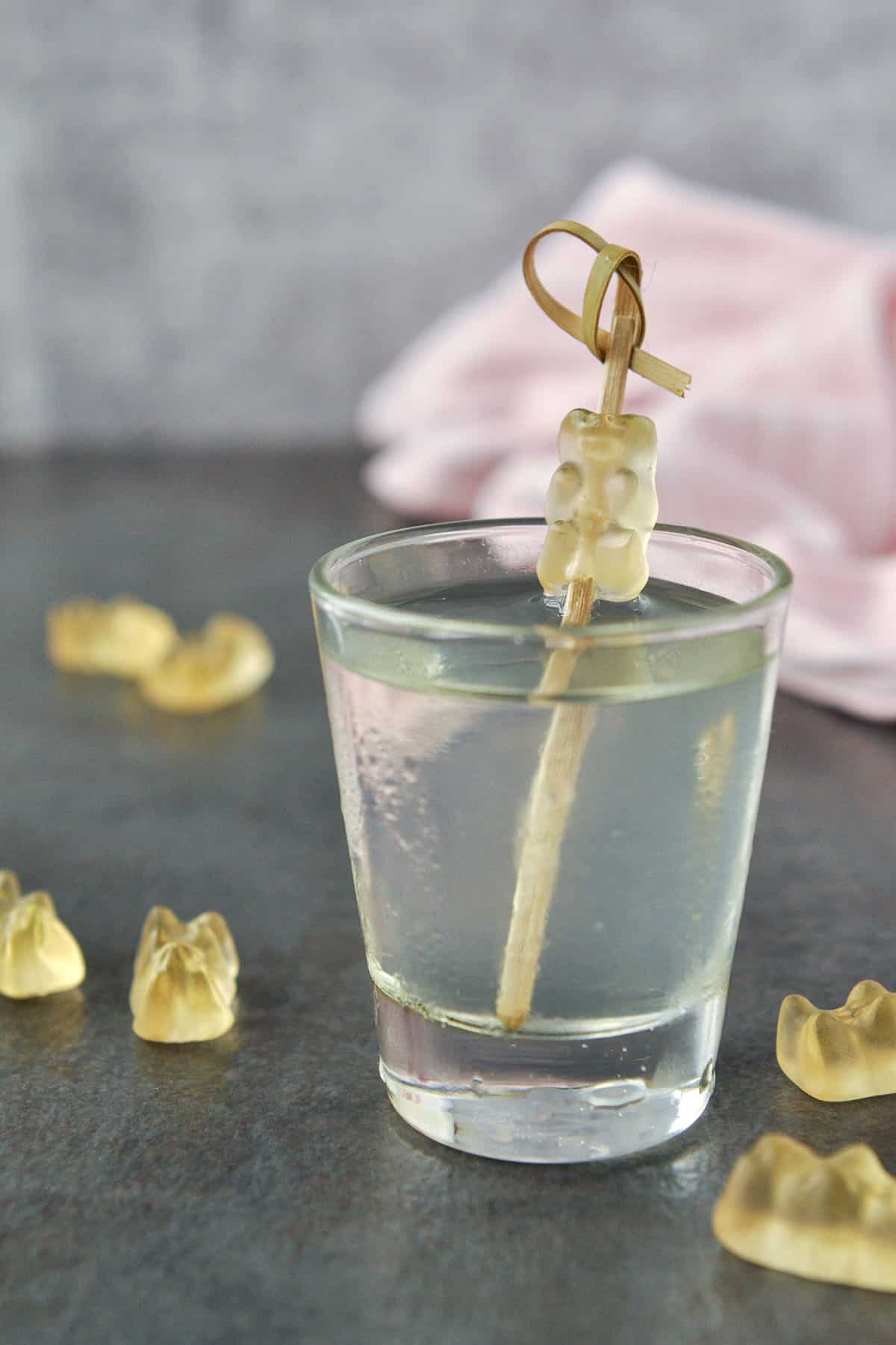 One gummy bear shot with a white gummy bear on a cocktail stick and pink towel in the background.