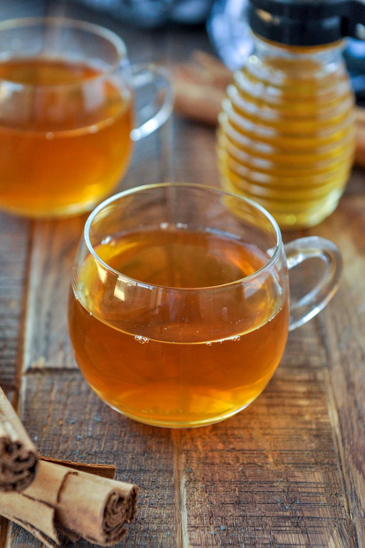 An up close of glass mugs of tea and a jar of honey in the background.