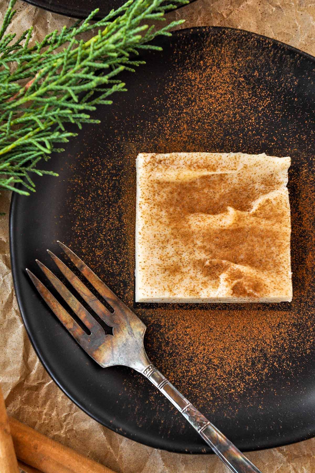 Above view of natilla on a black plate sprinkled with cinnamon.