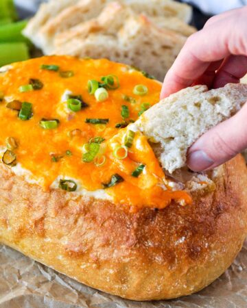 A piece of bread being dipped into a cheesy sin dip.
